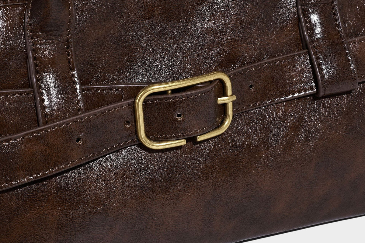 Strukturierte dunkelbraune Henkeltasche mit Öl-Wachs-Finish, vorderer Gürtelschnalle, goldfarbenen Beschlägen und zwei Tragegriffen, Detailansicht