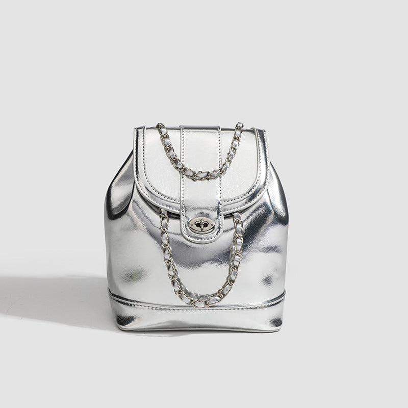 Kompakte silberfarbene Metallic-Rucksacktasche mit mehrfarbigen Kristallnieten, rundem Klappverschluss mit Drehverschluss und ineinander verflochtenem Silber