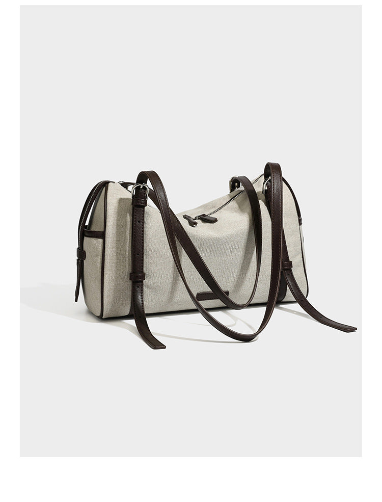 Beige canvas barrel bag with dark brown leather-look trim, silver-tone hardware, top zip closure, and adjustable shoulder