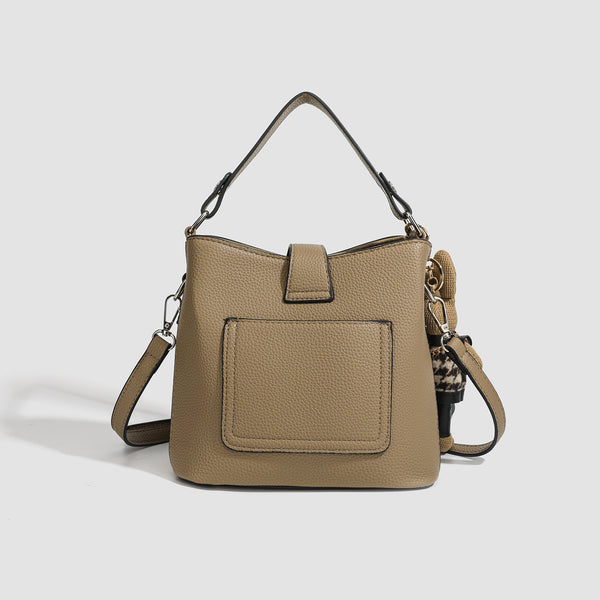 Structured taupe pebbled-texture bucket bag with top handle, silver ring hardware, tab-and-button closure, and knit bunny