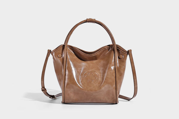 Glossy leather-look structured tote bag with rounded top handles, detachable shoulder strap, embossed front emblem, and side