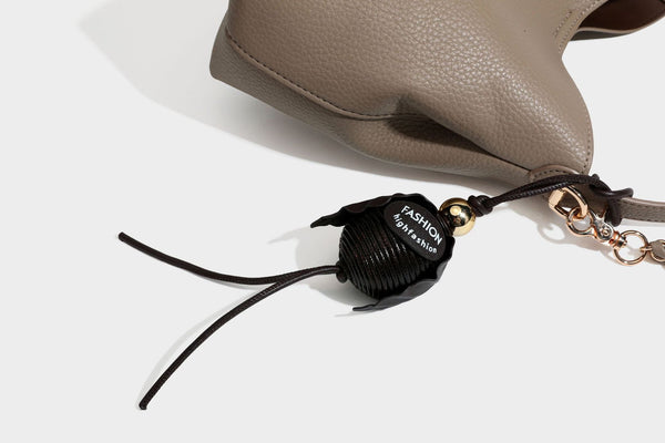 Schultertasche in genarbter Lederoptik im Hobo-Stil mit goldfarbener Kette, kurzem Tragegriff und dekorativem Anhänger an der Seite, Detailansicht
