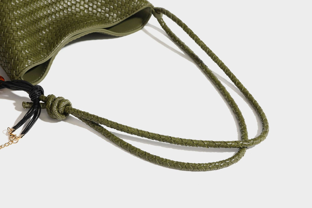 Olive green woven leather-look bucket bag with braided crossbody strap, knotted adjustment, and gold-tone tassel charm with