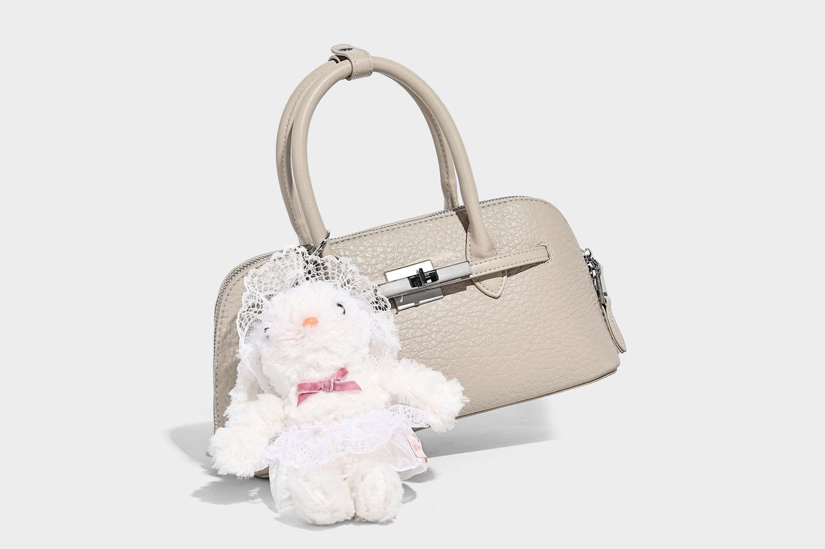 Small structured shell-silhouette top-handle bag with pebbled leather-look finish, silver-tone turn-lock hardware, and