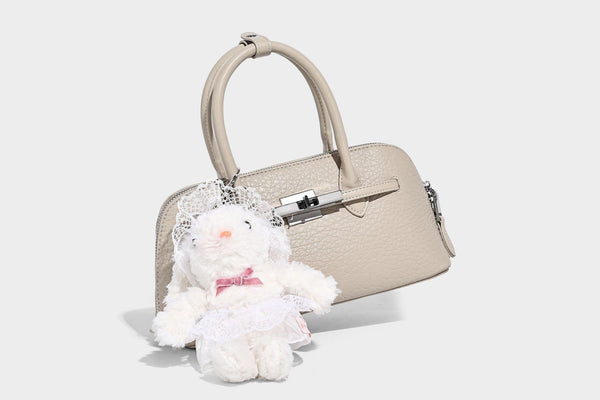 Small structured shell-silhouette top-handle bag with pebbled leather-look finish, silver-tone turn-lock hardware, and