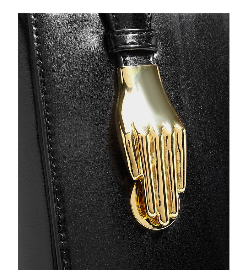 Kleine, strukturierte, kastenförmige Henkeltasche mit goldfarbenem, handförmigem Metallbeschlag in schwarzer Lederoptik mit abnehmbarem Detail