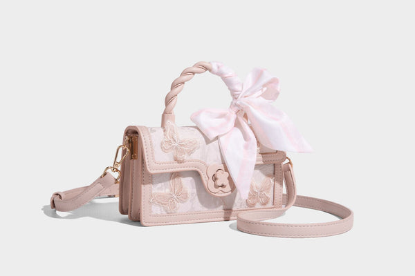 Small structured white flap bag with butterfly embroidery, flower-shaped turn-lock clasp, braided top handle with scarf bow