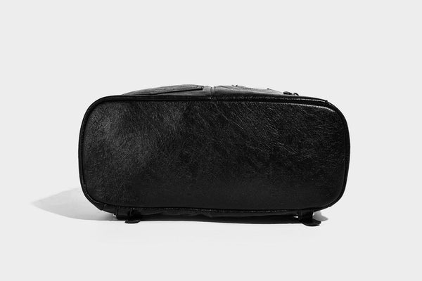 Glossy black convertible bucket backpack with silver grommet-studded straps, drawstring cinch closure, and front zip pocket