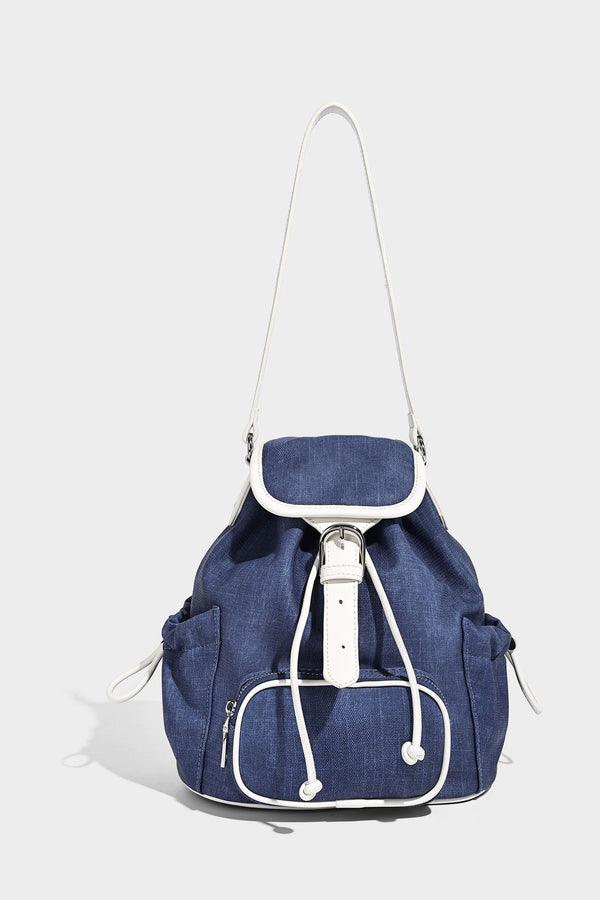 Compact denim drawstring backpack with white leather-look piping, flap-top buckle closure, front zip pocket, and silver-tone