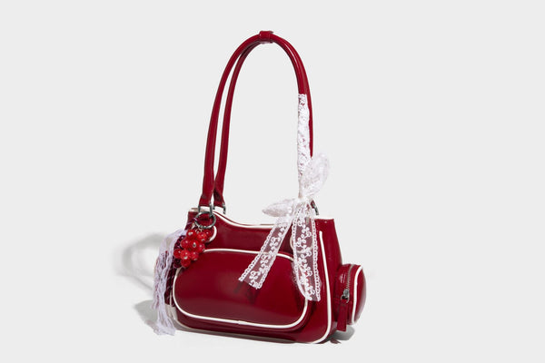 Kleine, formstabile, glänzende Schultertasche mit weißer Paspelierung, Spitzenschleife und Anhänger mit roter Perle, seitlichen Reißverschlusstaschen und silberfarbenem