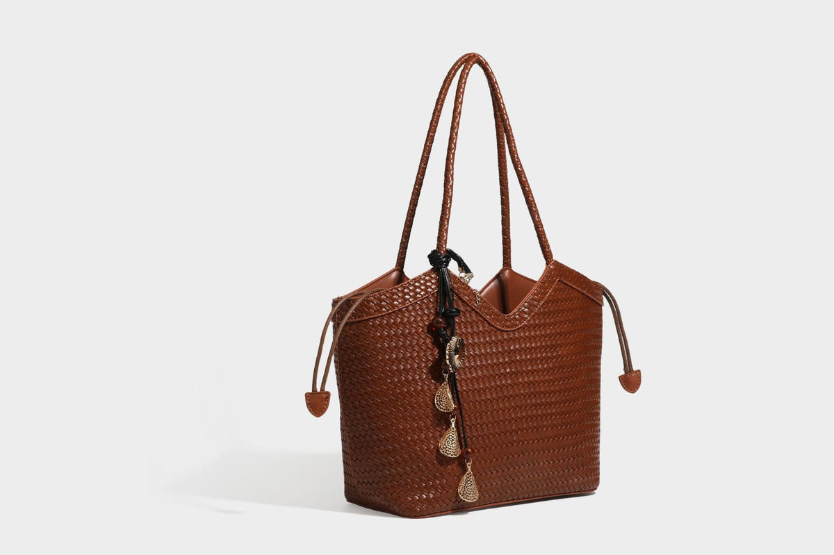 Olivgrüne Tote-Bag in Korbgeflecht-Optik mit dunkelbraunen geflochtenen Schulterriemen, seitlichen Kordelzügen und Perlenanhänger in Goldoptik