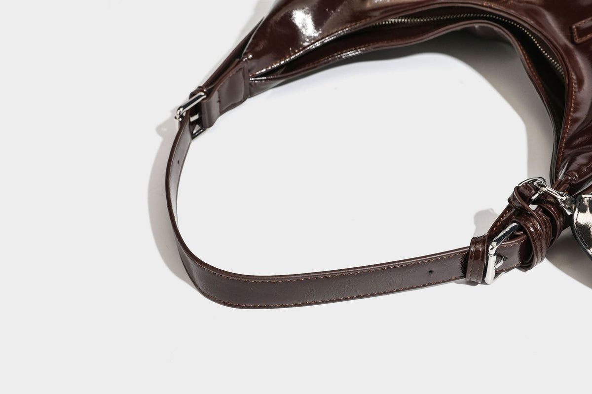 Glänzende dunkelbraune, lässig geschnittene Hobo-Schultertasche mit Riemendetail mit silberfarbenen Ösen, Reißverschlussfach auf der Vorderseite und Herz mit Leopardenmuster