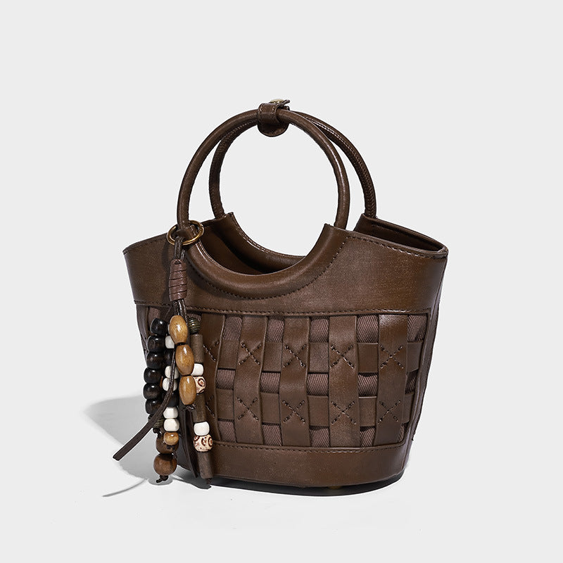 Small woven-panel bucket bag with circular ring handles, beaded tassel charm, and detachable crossbody strap in brown, detail