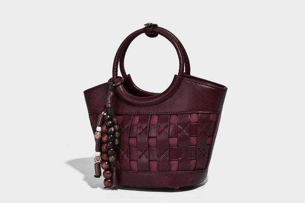 Small woven-panel bucket bag with circular ring handles, beaded tassel charm, and detachable crossbody strap in brown, detail