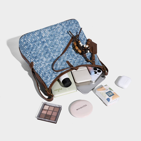 Light blue woven bucket bag with brown leather-look trim, gold-tone hardware, adjustable shoulder strap, and decorative bead
