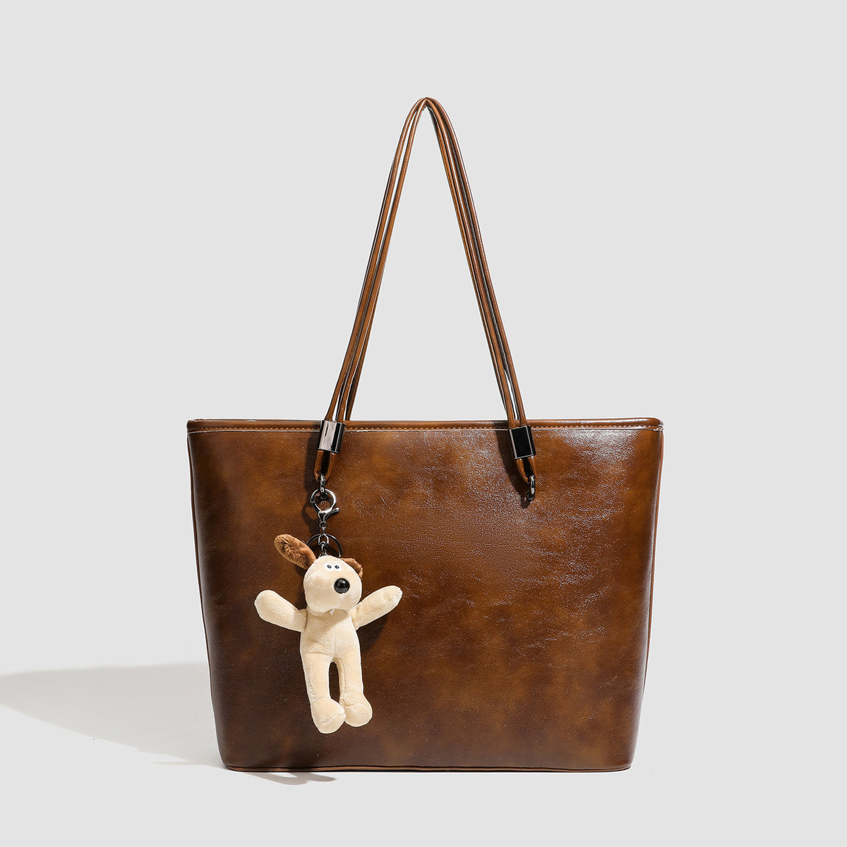Large structured brown vintage-finish tote bag with double shoulder handles, gunmetal hardware, and plush bear charm, front