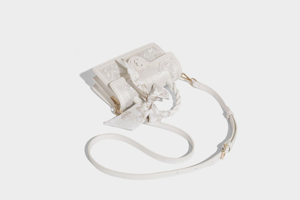 Small structured white flap bag with butterfly embroidery, flower-shaped turn-lock clasp, braided top handle with scarf bow