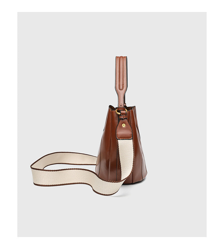 Smooth leather-look paneled bucket bag in brown with wide woven shoulder strap, gold-tone ring hardware, and detachable zip
