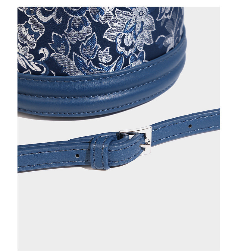 Small cylindrical barrel bag in blue-and-white floral jacquard with leather-look trim, scarf-wrapped top handle, silver-tone