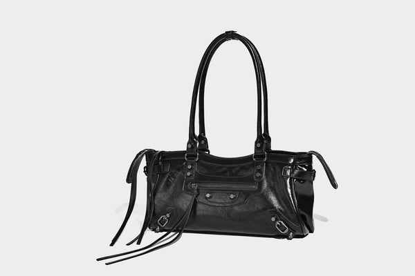 Längliche Schultertasche in Zylinderform mit glänzender Lederoptik, silberfarbenen Nietenbeschlägen, seitlichen Quasten und mehreren außenliegenden Reißverschlüssen