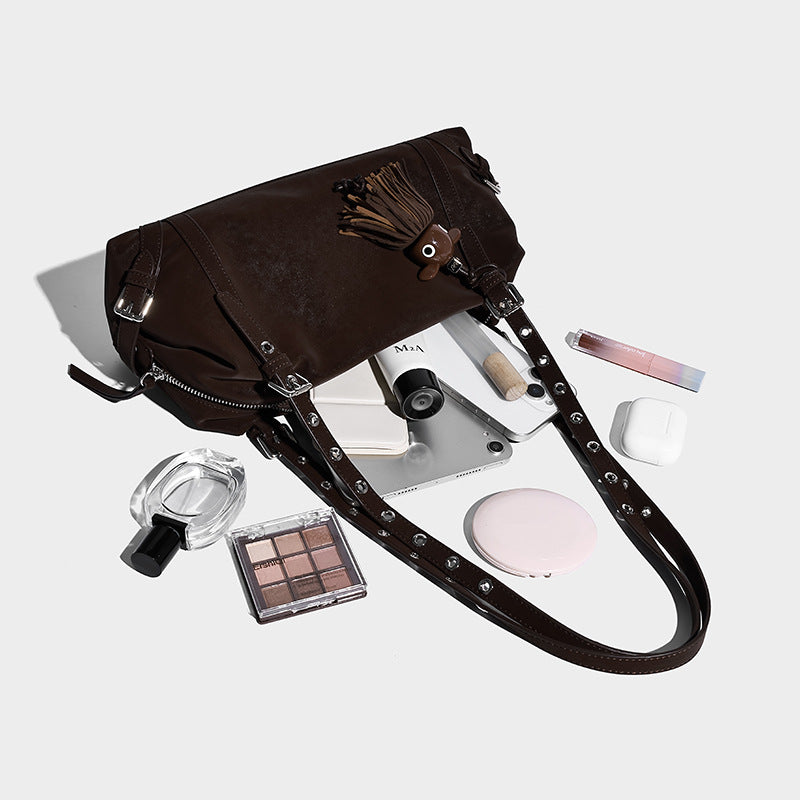 Lässige Barrel-Schultertasche in Dunkelbraun mit Riemen mit silberfarbenen Ösen, Reißverschluss oben, seitlichen Schnallenbeschlägen und Quaste