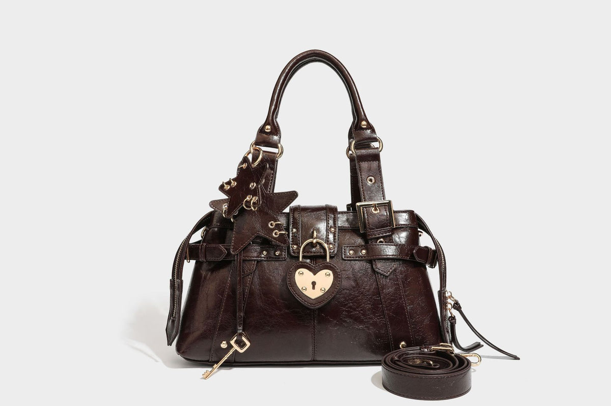 Structured leather-look satchel bag with heart padlock charm, star charm, gold-tone buckle hardware, dual top handles, and