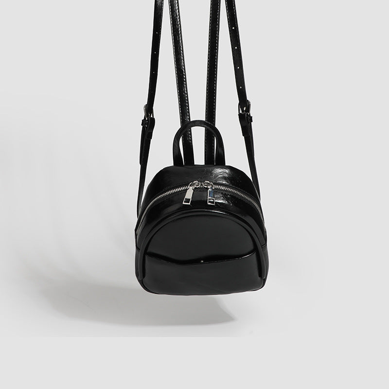 Kompakter, abgerundeter Mini-Rucksack im Lederlook mit glänzender Oberfläche, Reißverschluss oben, Vordertasche und Tragegriff oben, Detailansicht