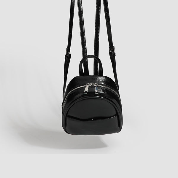 Kompakter, abgerundeter Mini-Rucksack im Lederlook mit glänzender Oberfläche, Reißverschluss oben, Vordertasche und Tragegriff oben, Detailansicht