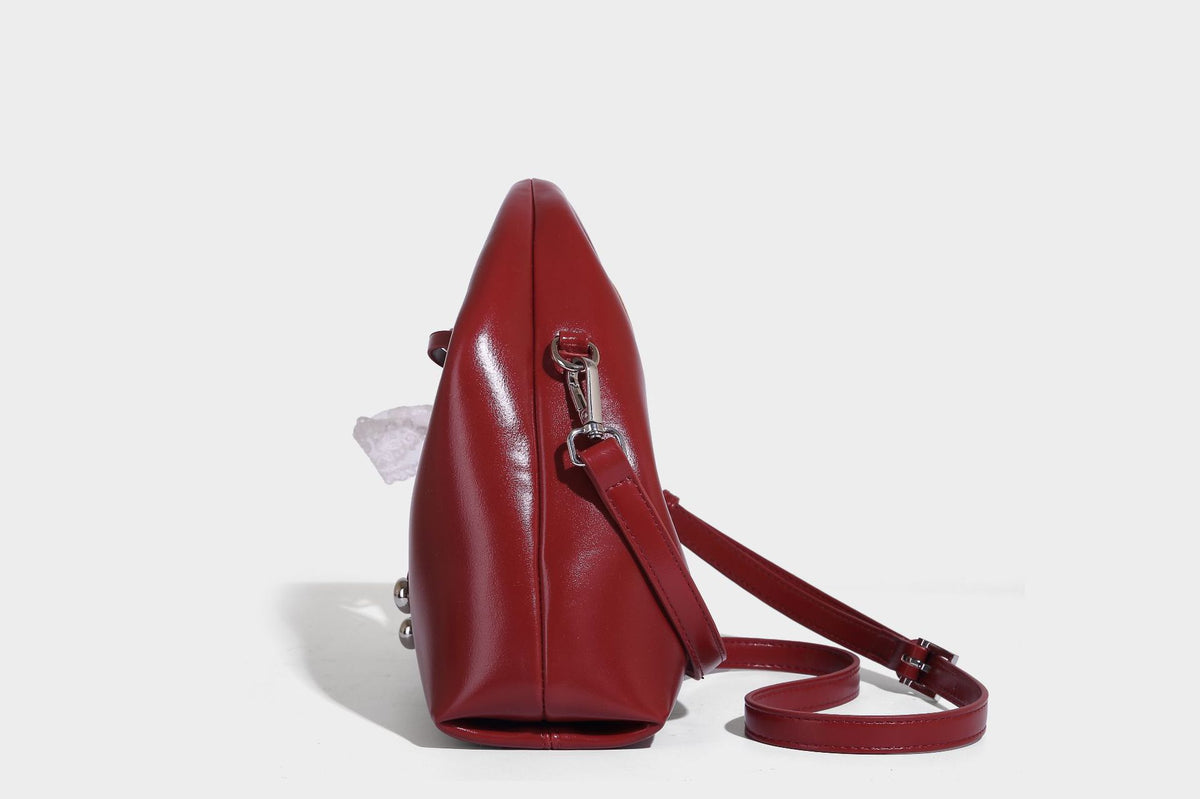 Kleine kuppelförmige Henkeltasche in glänzender Lederoptik mit Kordelzugverschluss, weißem Spitzen-Schleifenanhänger und silberfarbenen Metallbeschlägen