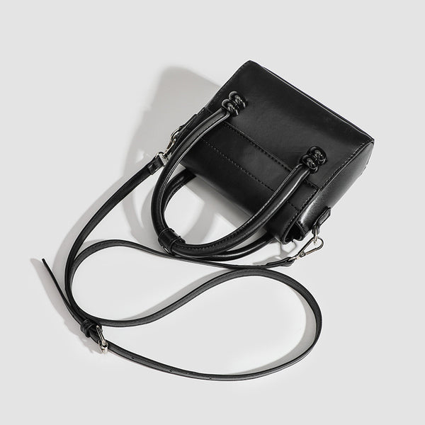 Kleine strukturierte schwarze Henkeltasche im Lederlook mit zwei abgerundeten Henkeln, abnehmbarem Umhängeriemen und silberfarbenem