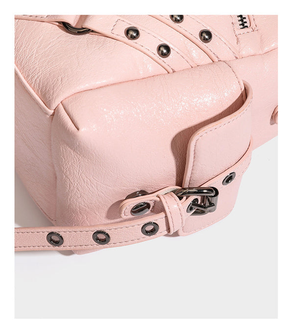 Structured pink leather-look satchel bag with gunmetal studded trim, rectangular buckle strap, dual top handles, and, detail