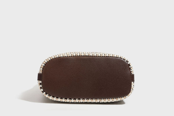 Woven stripe bucket shoulder bag in cream and dark brown with leather-look trim, knotted adjustable strap, and small shield