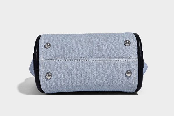 Light blue denim trapezoid tote bag with black leather-look trim, knotted top handles, detachable crossbody strap, front