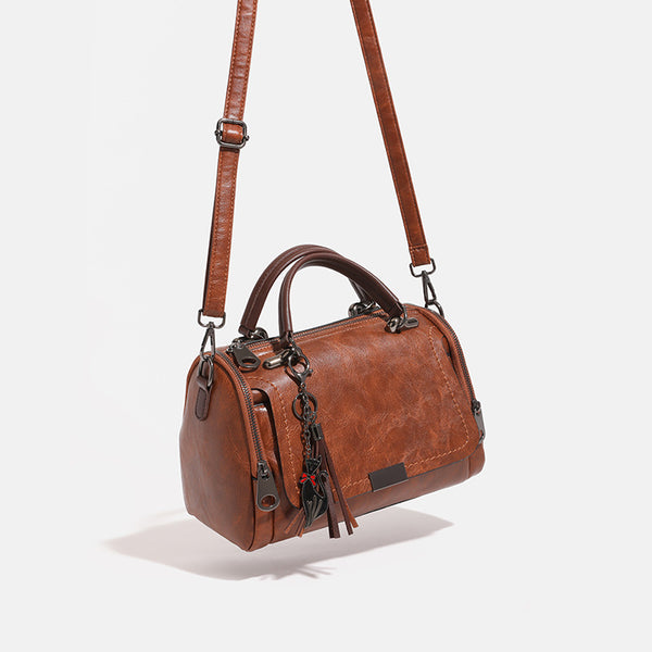 Compact structured barrel bag in distressed leather-look finish with dual top handles, detachable crossbody strap, front zip