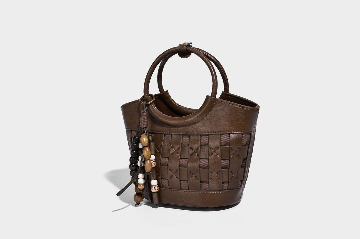 Small woven-panel bucket bag with circular ring handles, beaded tassel charm, and detachable crossbody strap in brown, detail
