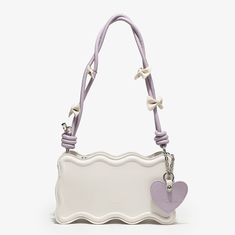 Small structured scalloped-edge shoulder bag with bow-tied pink cord strap and silver heart charm pendant, front view