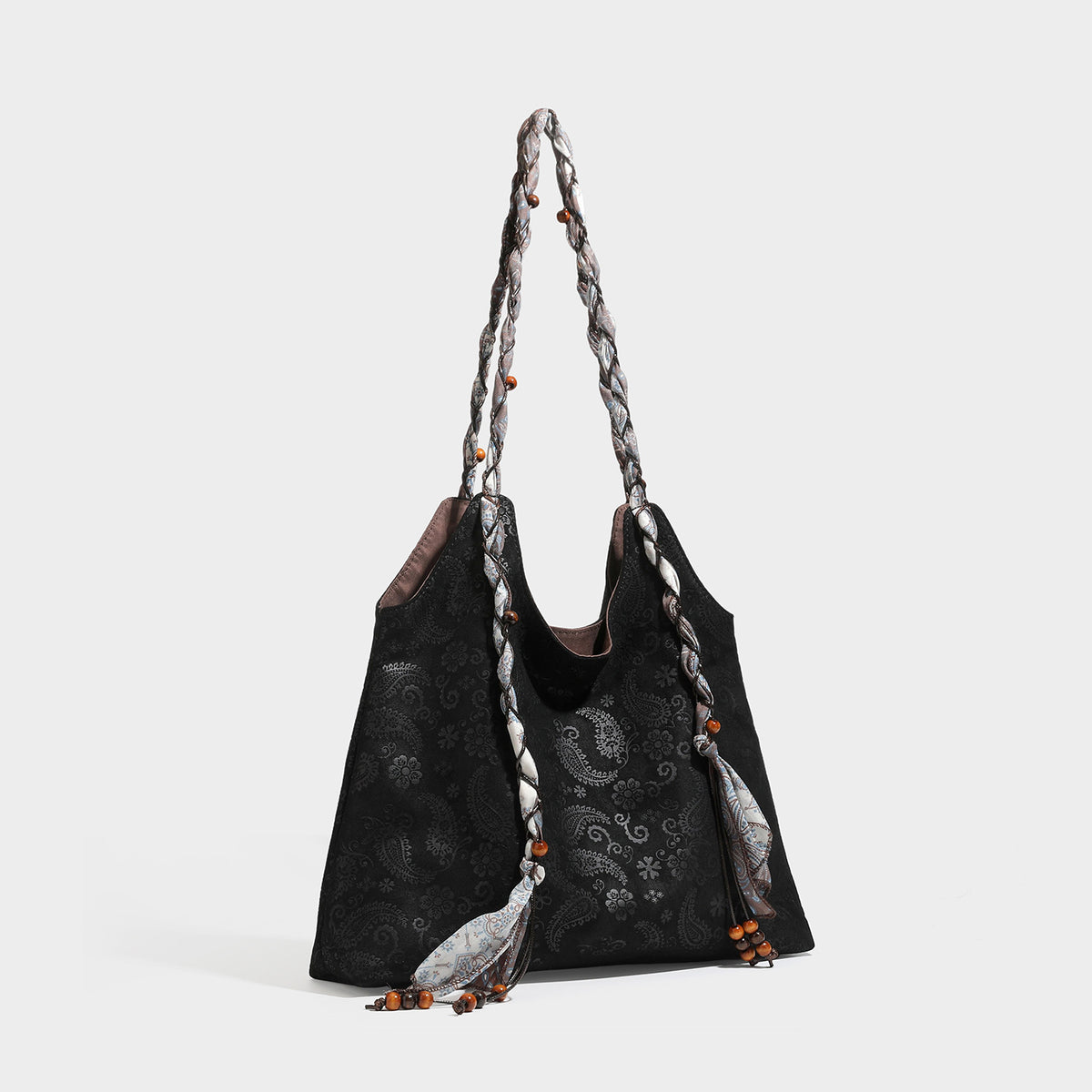 Slouchy paisley-embossed suede-look shoulder tote bag with braided patterned fabric straps and wood bead accents, detail view
