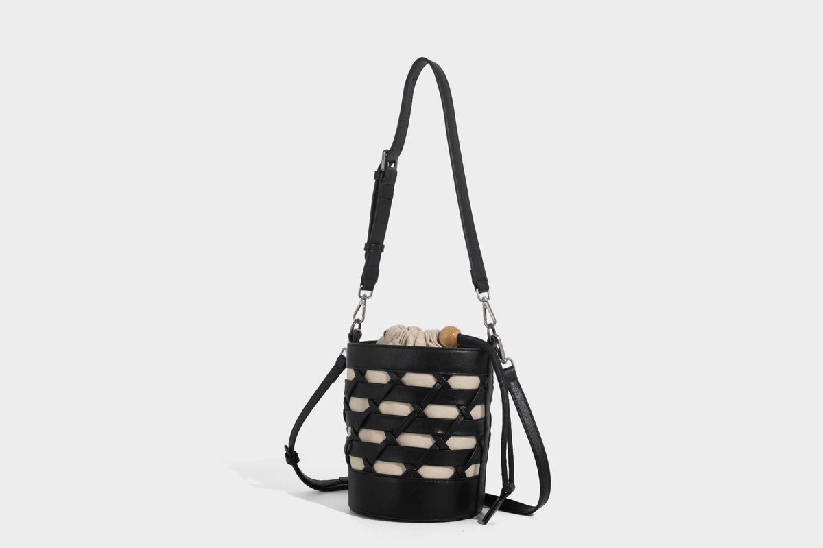 Small cylindrical woven lattice bucket bag with leather-look black trim, beige canvas body, wooden bead drawstring closure
