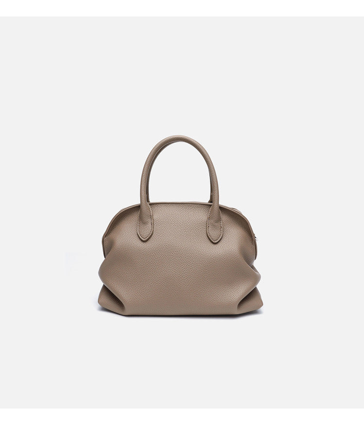 Rounded dome shell handbag in pebbled leather-look finish with twin top handles, zip closure, decorative horse charm, and