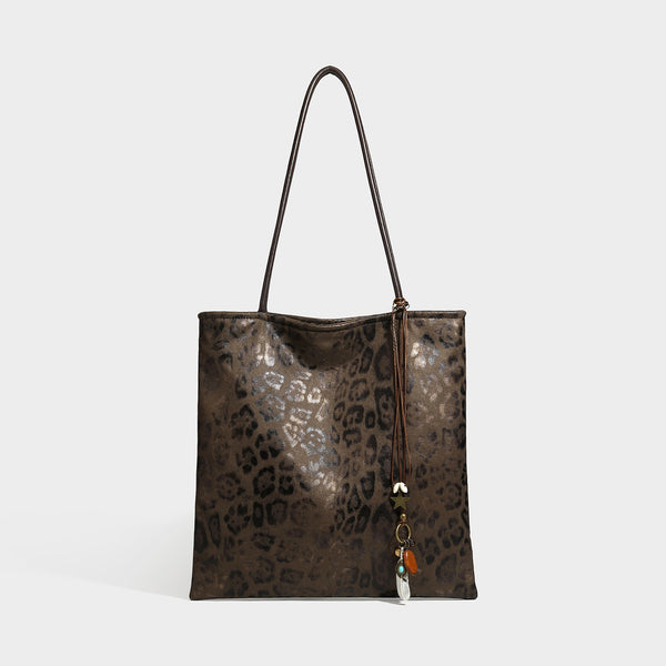 Large leopard print shoulder tote bag in tan and brown with slim dark straps and dangling beaded charm hardware, detail view