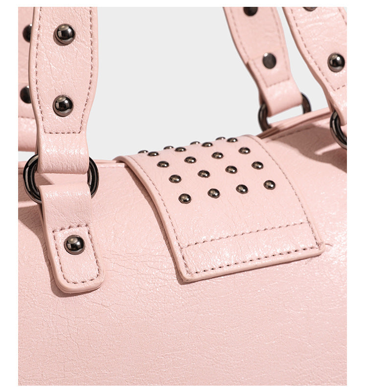 Structured pink leather-look satchel bag with gunmetal studded trim, rectangular buckle strap, dual top handles, and, detail