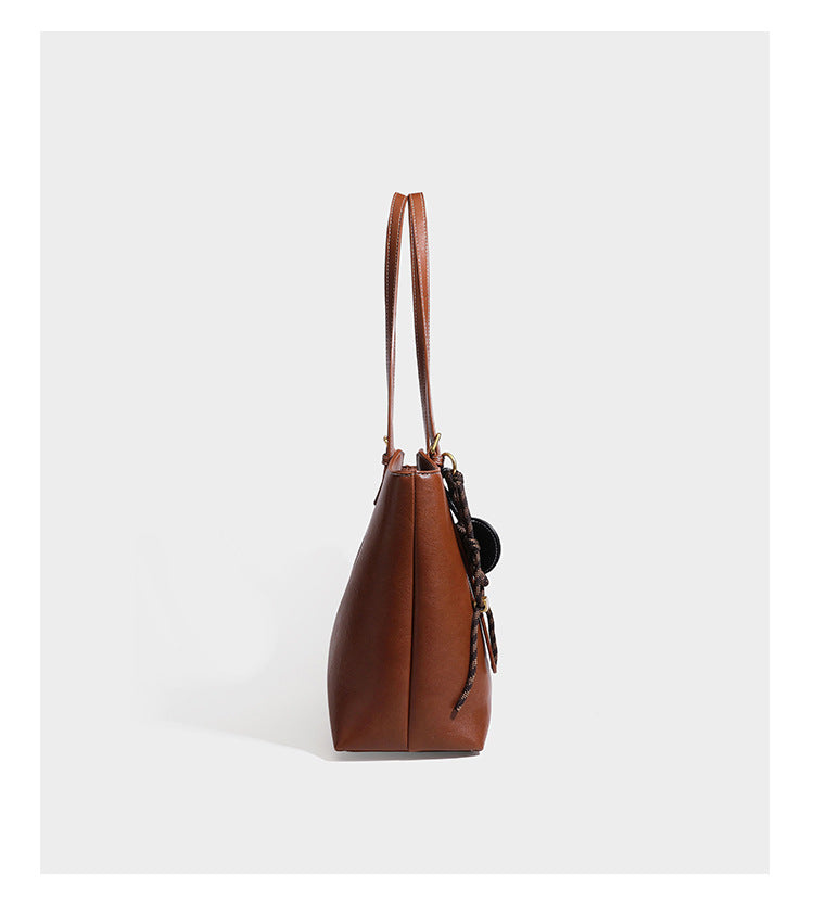 Structured smooth leather-look tote bag with long shoulder strap, gold-tone hardware, and hanging tassel-coin charm, detail