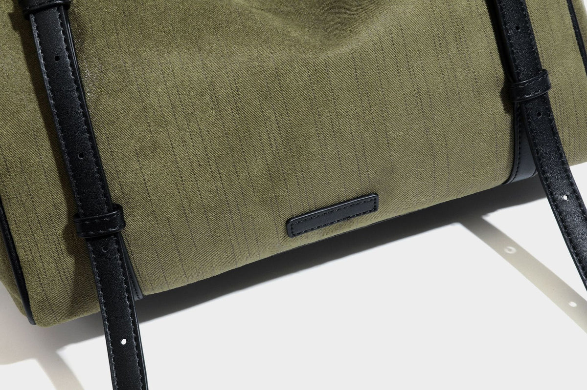 Olivgrüne Canvas-Schultertasche in Zylinderform mit schwarzen Trägern in Lederoptik, Reißverschluss oben und silberfarbenen Metallbeschlägen, Detailansicht