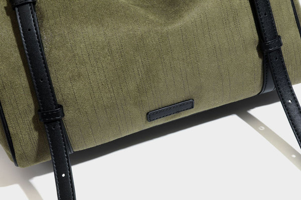 Olivgrüne Canvas-Schultertasche in Zylinderform mit schwarzen Trägern in Lederoptik, Reißverschluss oben und silberfarbenen Metallbeschlägen, Detailansicht