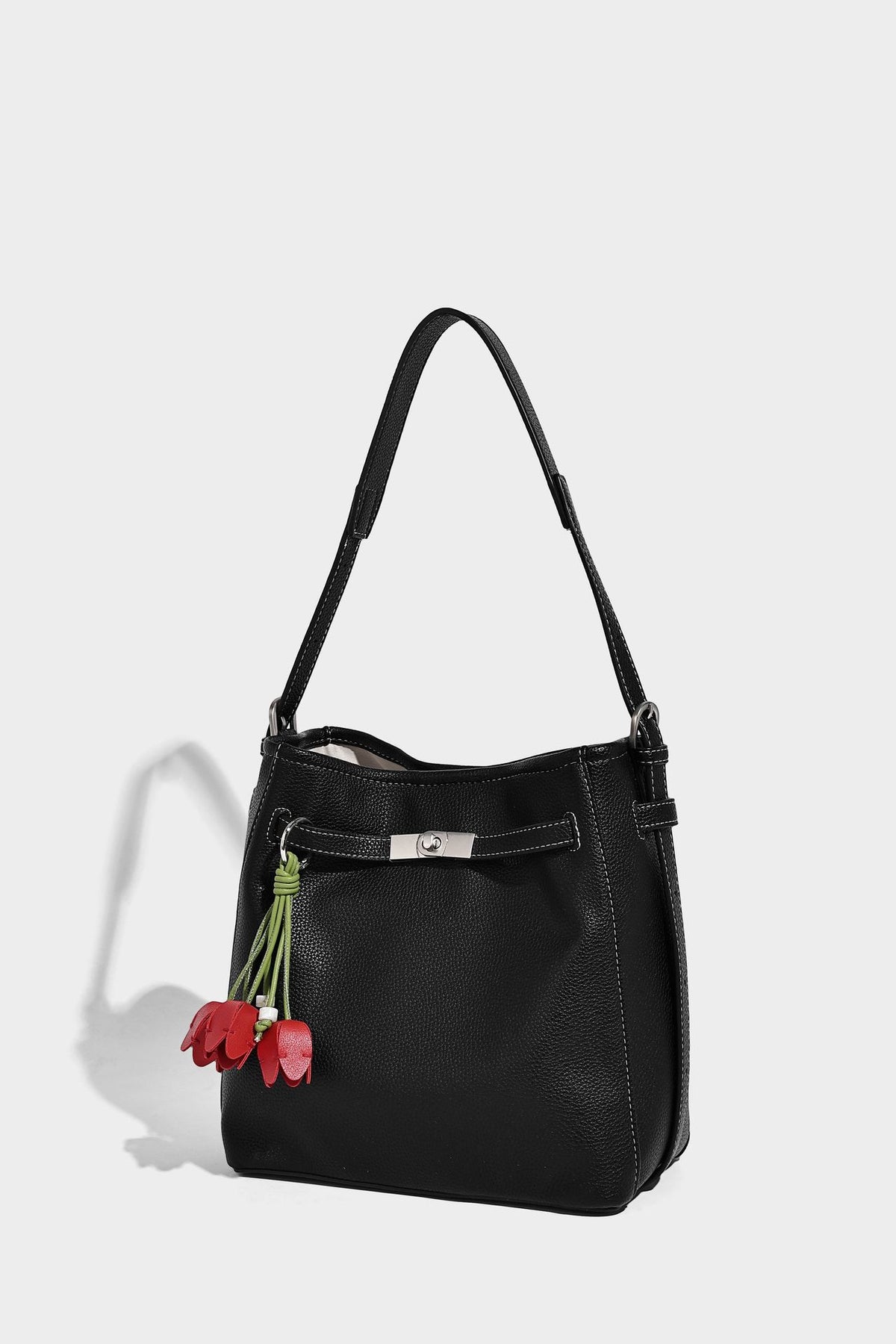 Soft-structured pebbled bucket shoulder bag with front turn-lock strap detail, adjustable strap, and hanging floral tassel