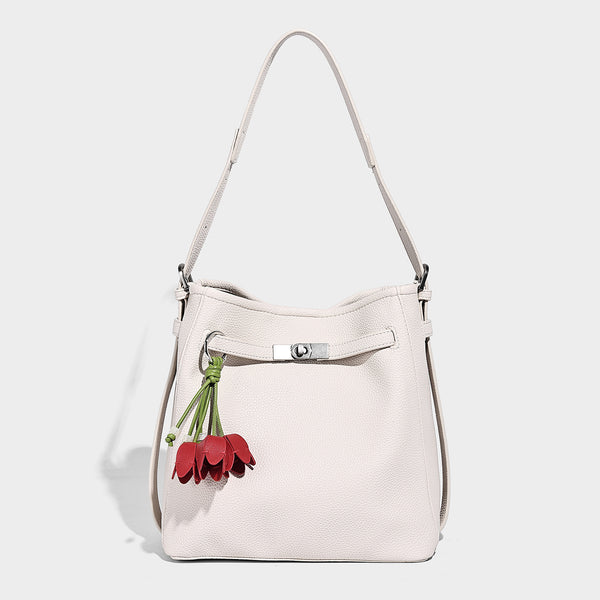 Soft-structured pebbled bucket shoulder bag with front turn-lock strap detail, adjustable strap, and hanging floral tassel
