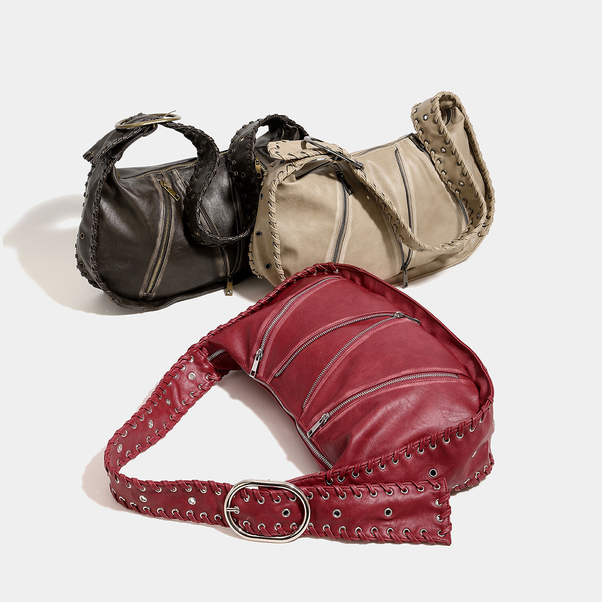 Slouchy hobo shoulder bag with wide braided eyelet strap, multiple front zip compartments, and silver-tone ring buckle