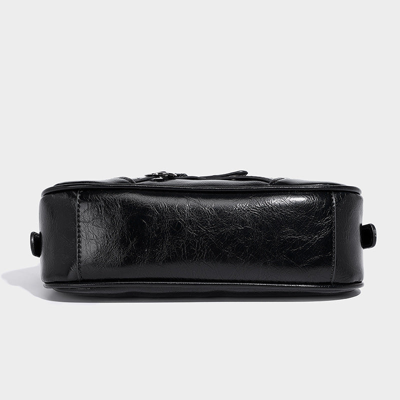 Compact moto-inspired shoulder bag with crisscross grommet strap detail, glossy textured finish, and adjustable crossbody