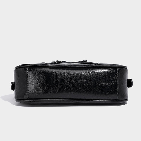Compact moto-inspired shoulder bag with crisscross grommet strap detail, glossy textured finish, and adjustable crossbody