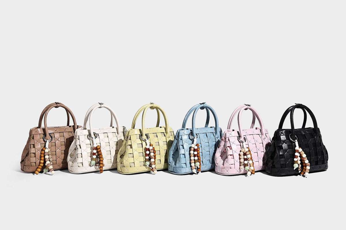 Small structured woven satchel tote with rounded top handles, silver-tone ring hardware, and bead tassel charm, detail view